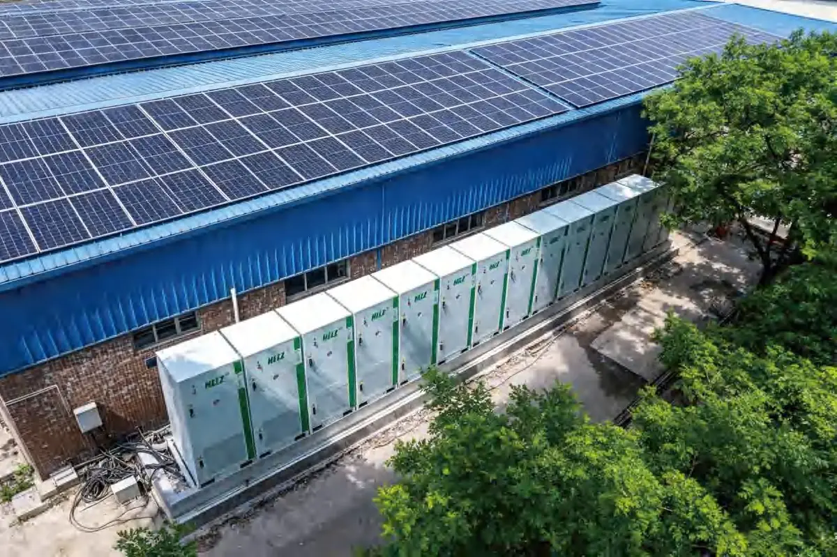 HELZ E100 battery cabinets in a row beside a blue-roof fasteners factory with rooftop PV